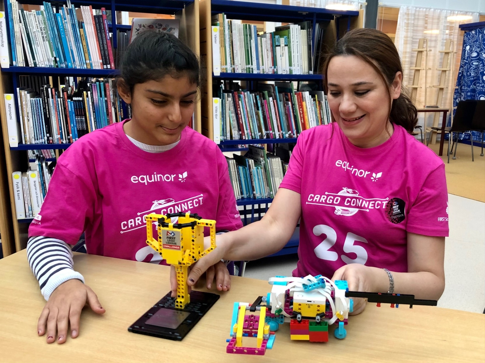 en flicka och en kvinna i rosa t-shirts tittar på en robot och en pokal
