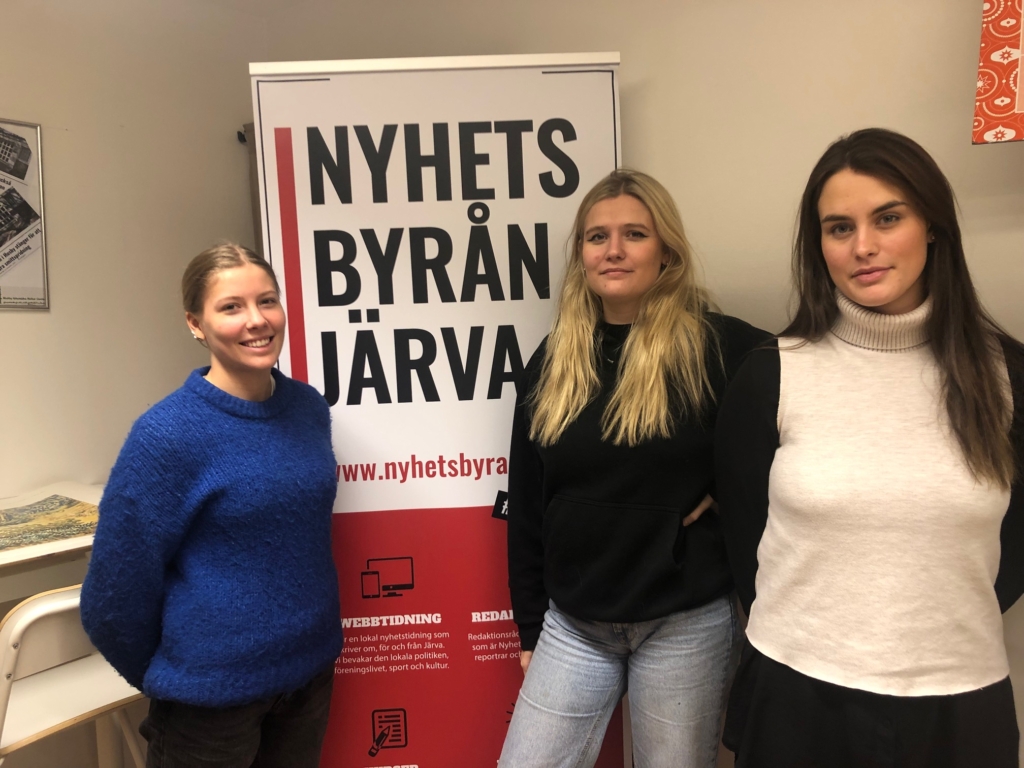 tre unga kvinnor framför Nyhetsbyrån Järvas roll-up
