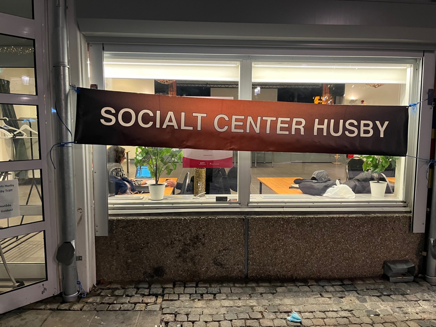 En banderoll med texten Socialt center Husby sitter på fönstret till Folkets Husby.