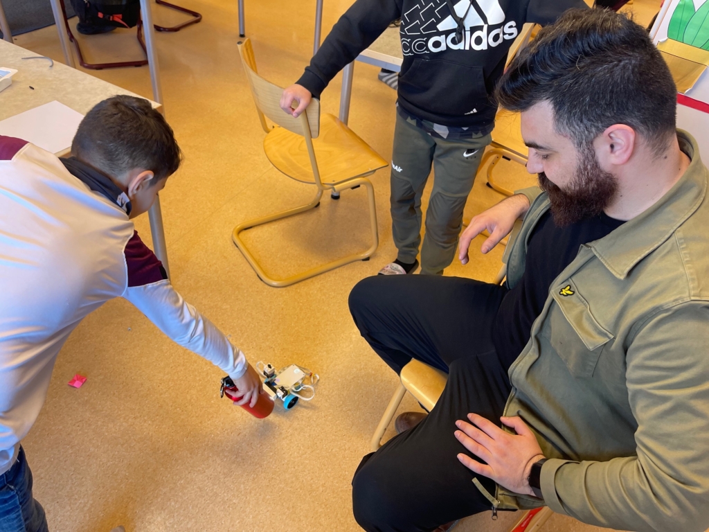 två barn och en vuxen testar en liten robot på golvet