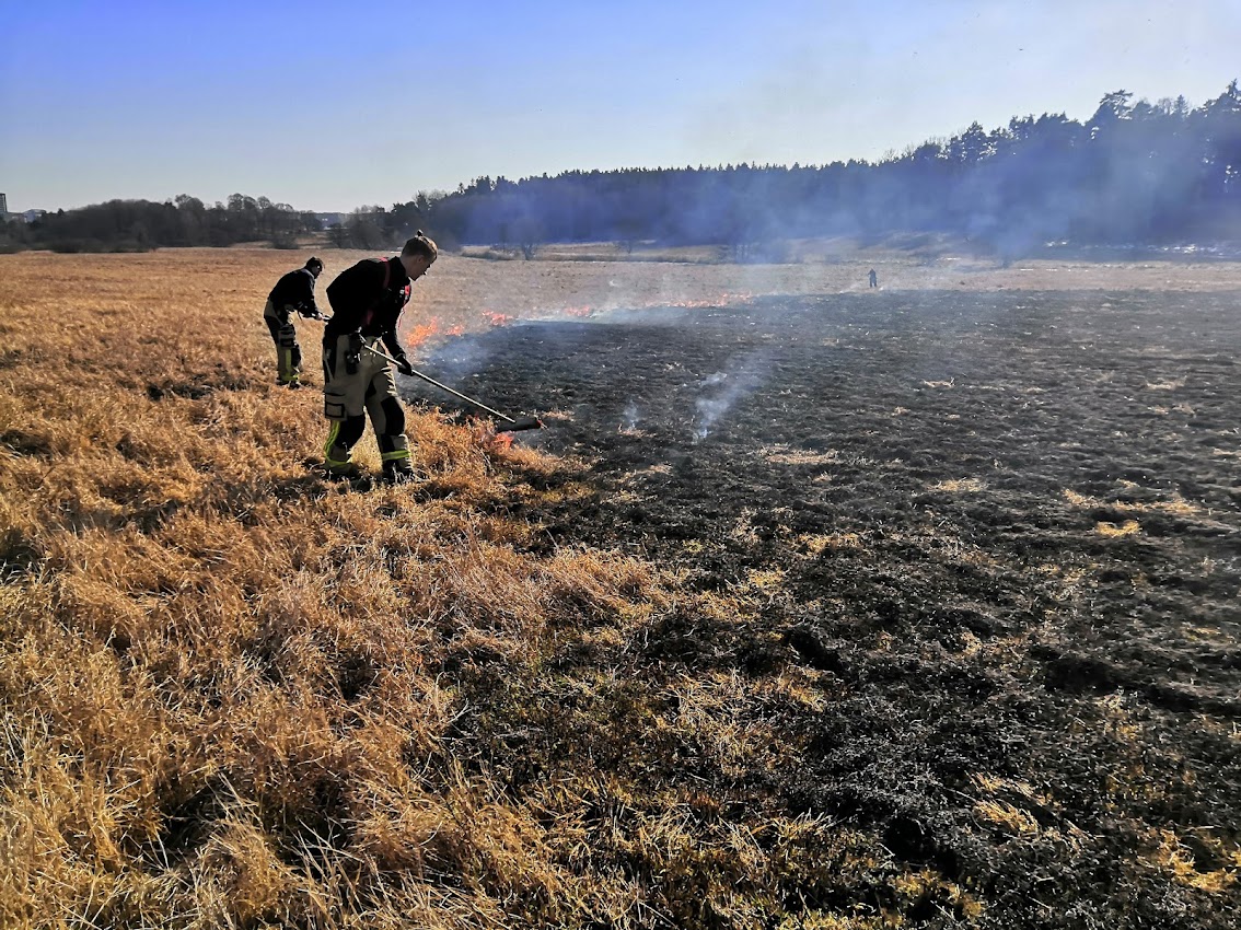 Brandmän släcker gräsbrand ute på Järvafältet.
