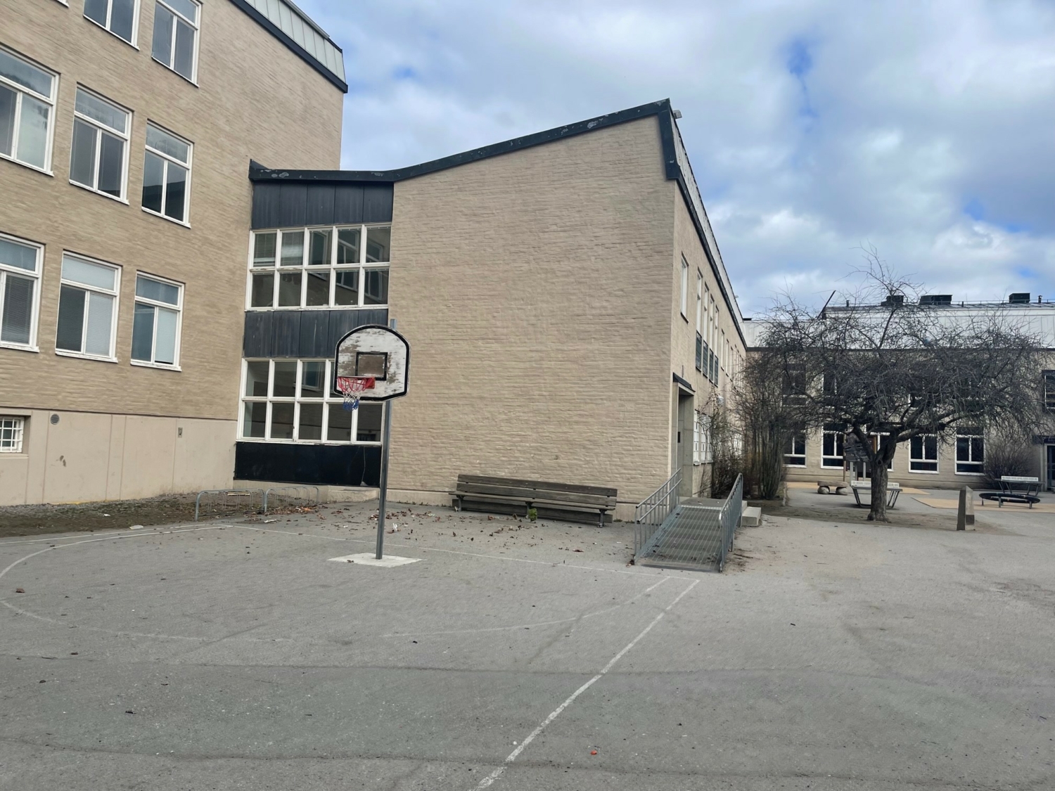 grå skolbyggnad med en basketkorg framför