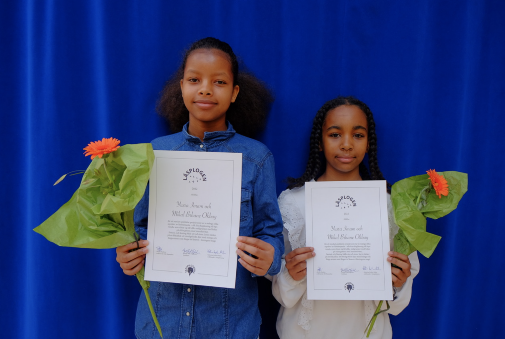 Två flickor håller diplom och blommor