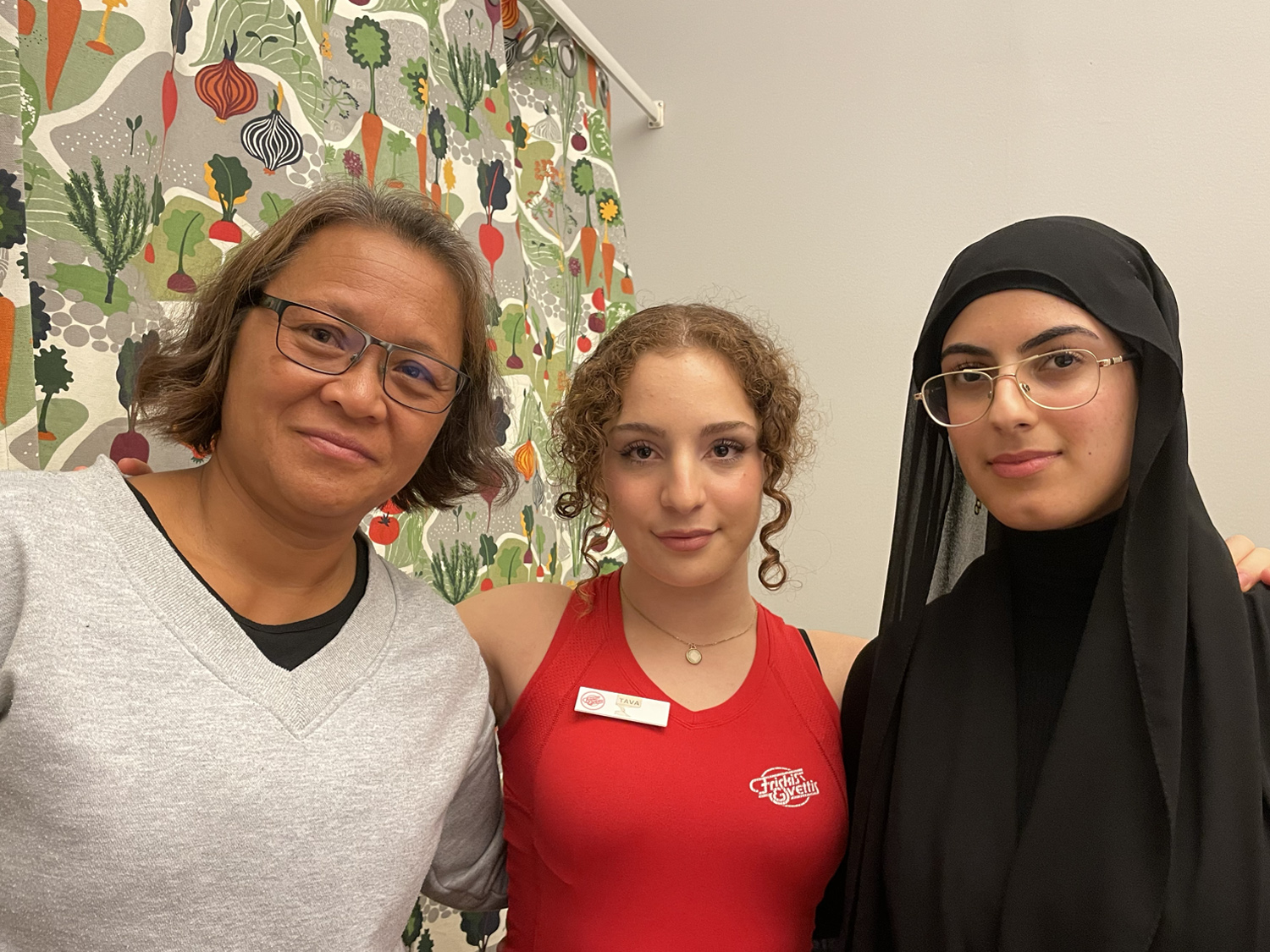 tre kvinnor, varav en i hijab och en i träningskläder, står bredvid varandra
