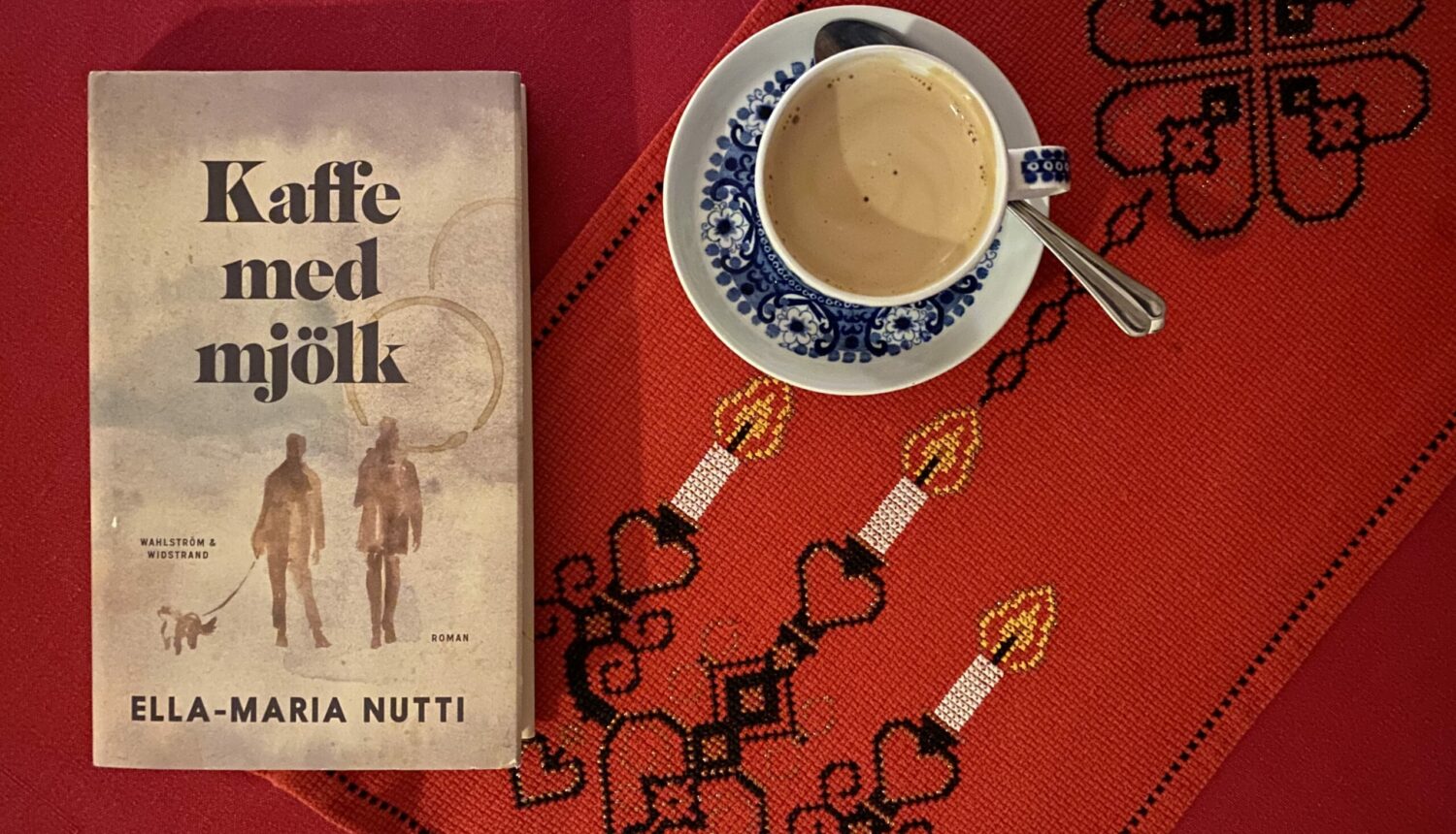 Boken Kaffe med mjölk på ett bord med julduk och en kopp kaffe.