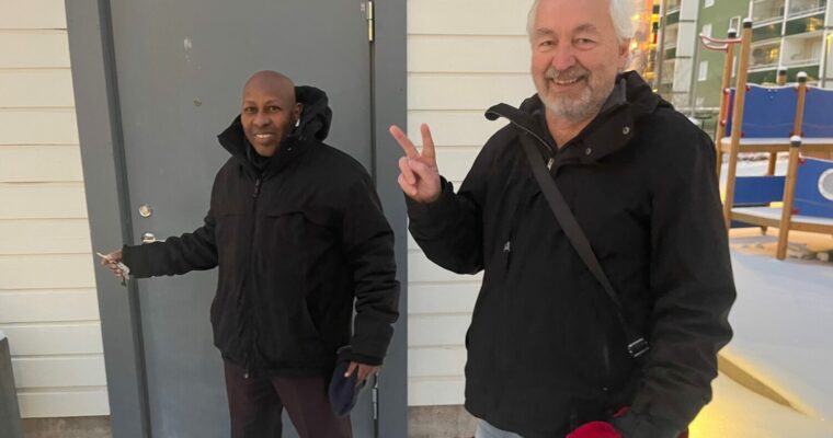 Två medelålders män står glada utanför en dörr