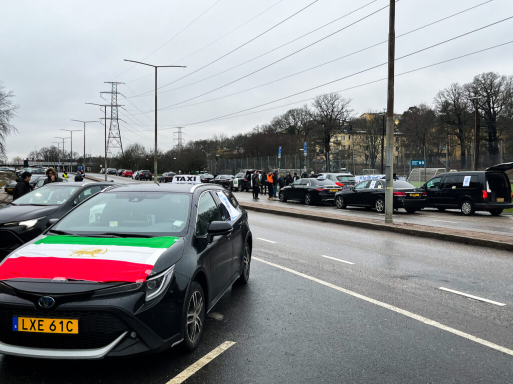 Bilar med plakat på led i protest. En har Kurdistans flagga på bilhuven.
