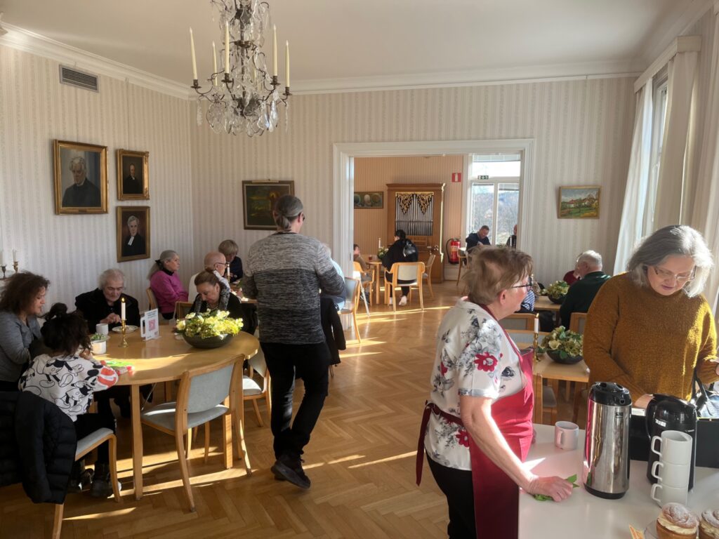 Rummet i prästgården där folk sitter vid flera bord och fikar.