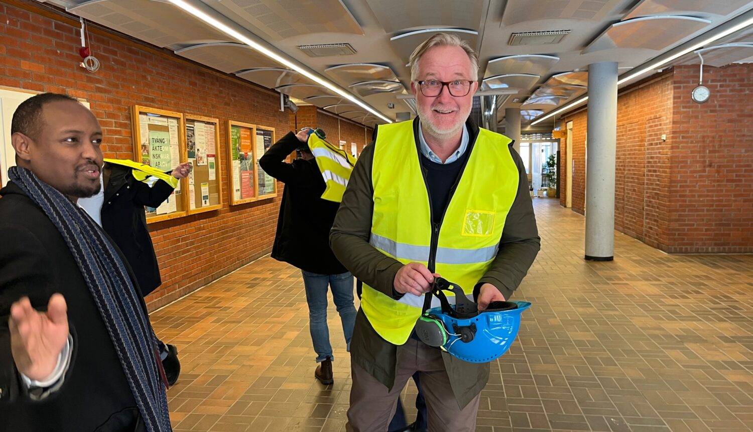 Leende man i gul väst och med en bygghjälm i handen.