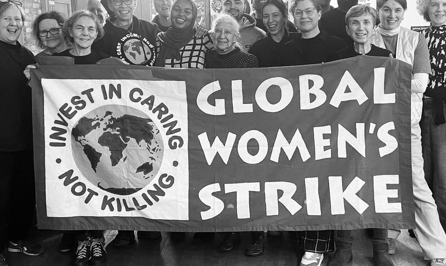 En svartvit bild med många människor bakom en banderoll. Texten Global Women's strike.
