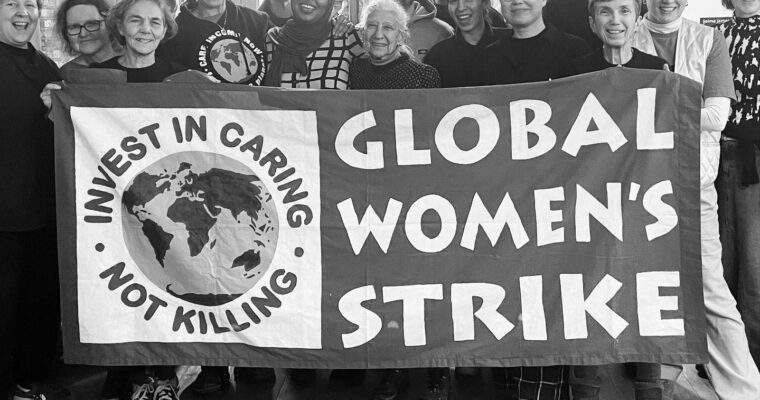 En svartvit bild med många människor bakom en banderoll. Texten Global Women's strike.