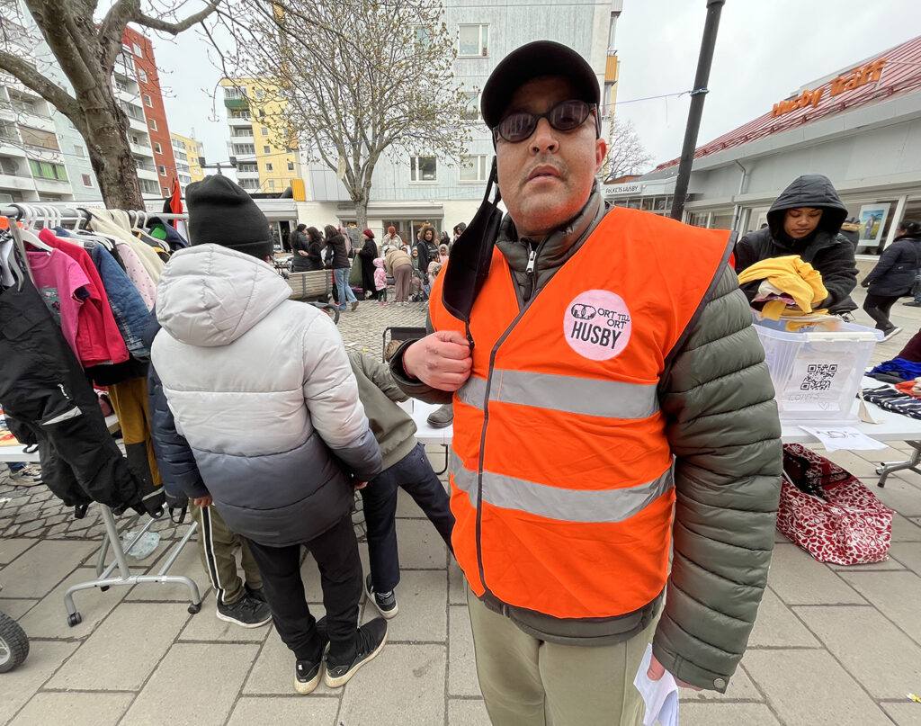 man i orange väst och svart keps framför marknadsstånd