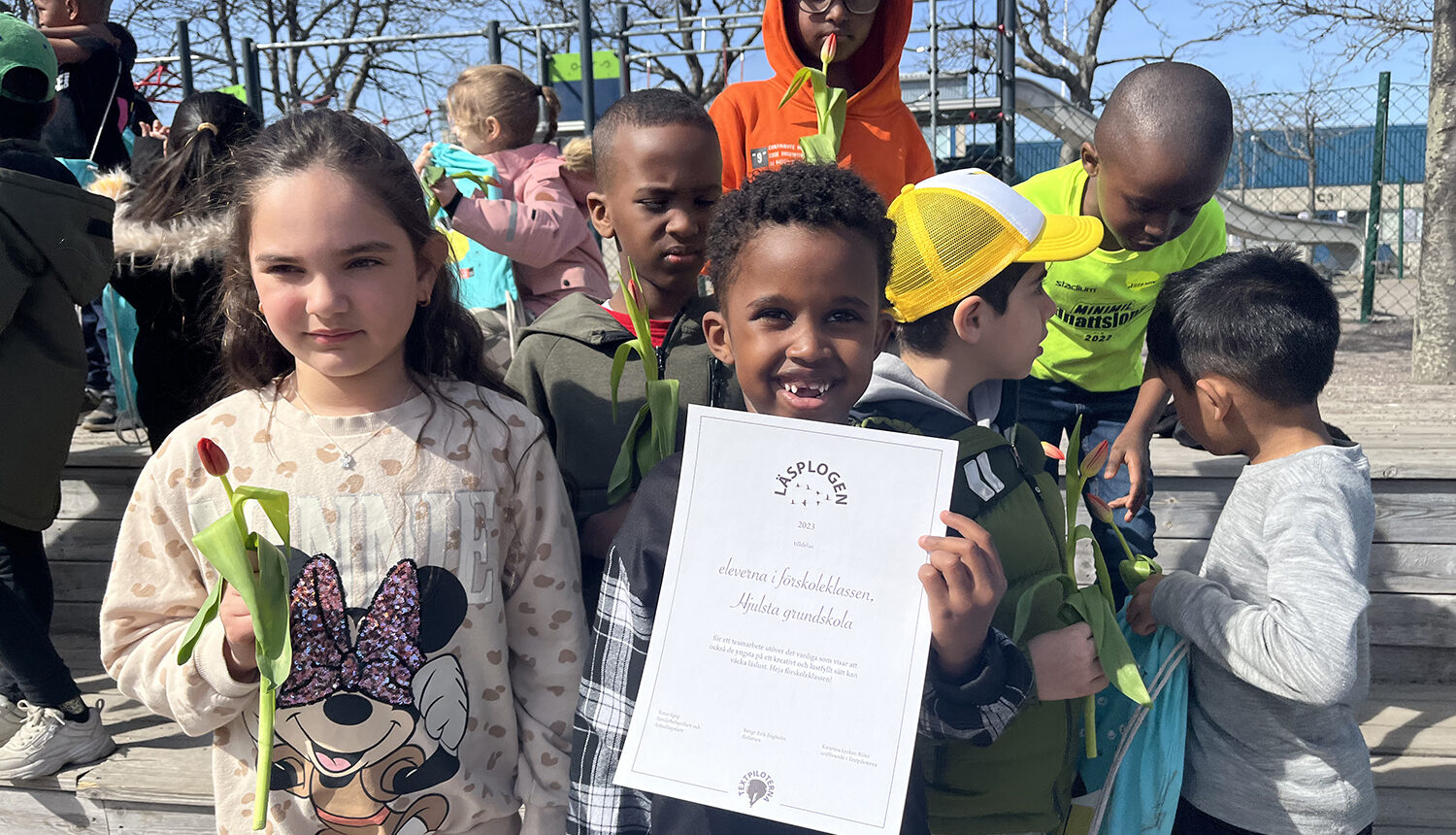 barn som håller blommor och ett diplom för läsfrämjandepriset Läsplogen