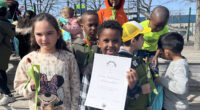 barn som håller blommor och ett diplom för läsfrämjandepriset Läsplogen