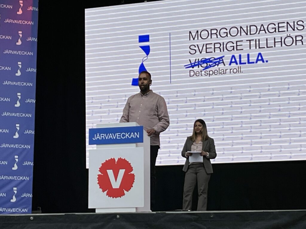 Vänsterpartiets Ilyas Hassan på Järvaveckans huvudscen. Partiledare Nooshi Dadgostar står i bakgrunden.