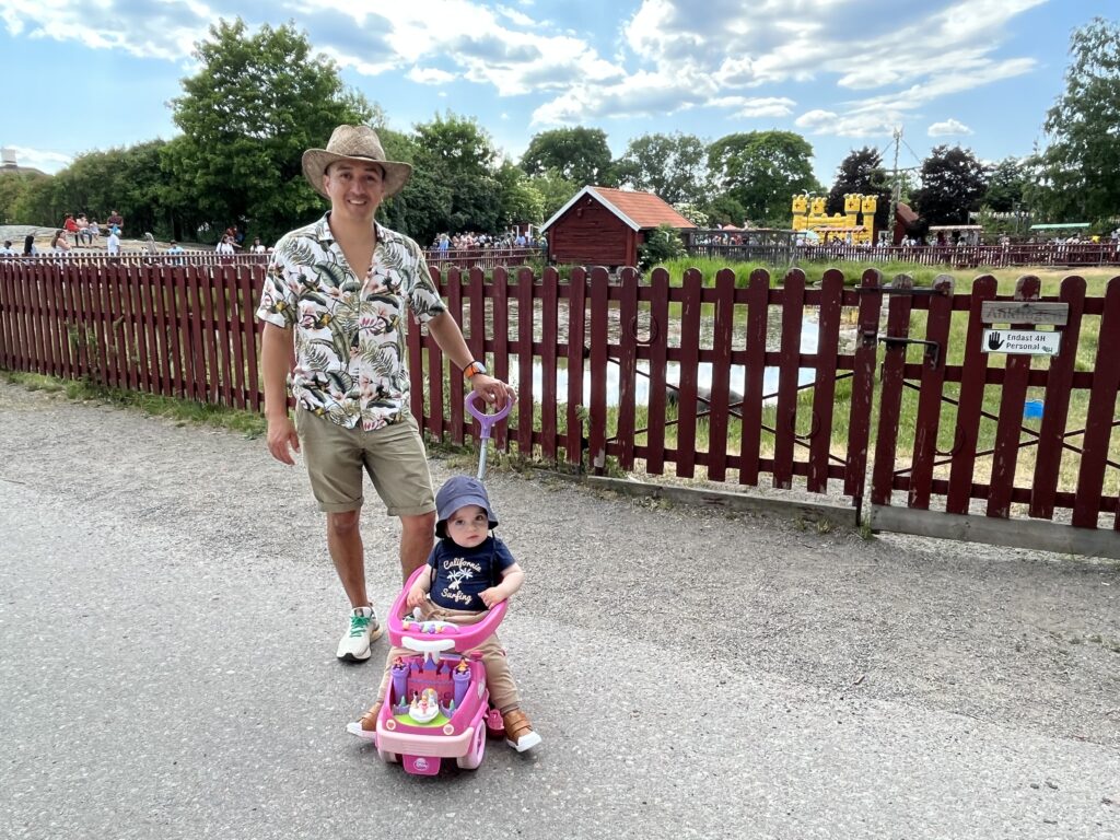 en man i hatt och en pojke på en leksaksbil står framför ett rött staket