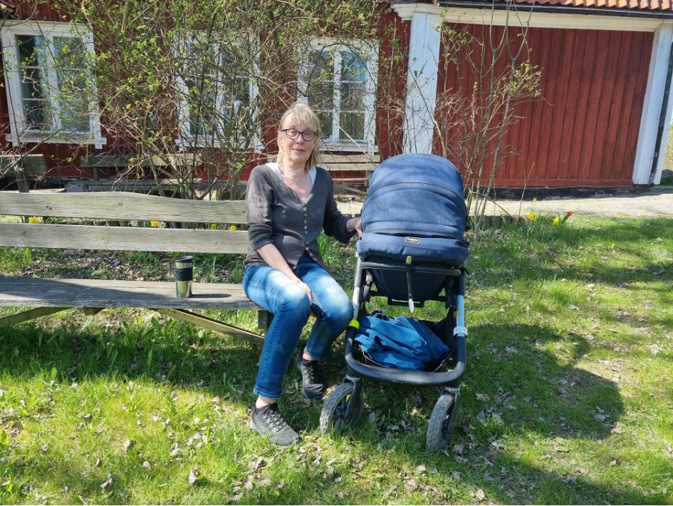 Kvinna sitter på en bänk med en barnvagn.