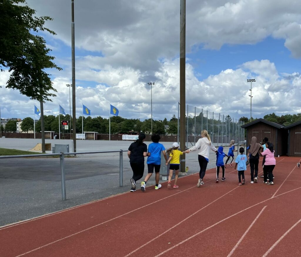 En grupp barn och en ledare som springer på löparbana utomhus