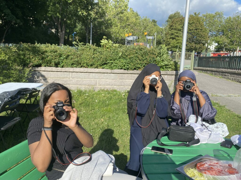 Tre unga kvinnor fotograferar med varsin kamera