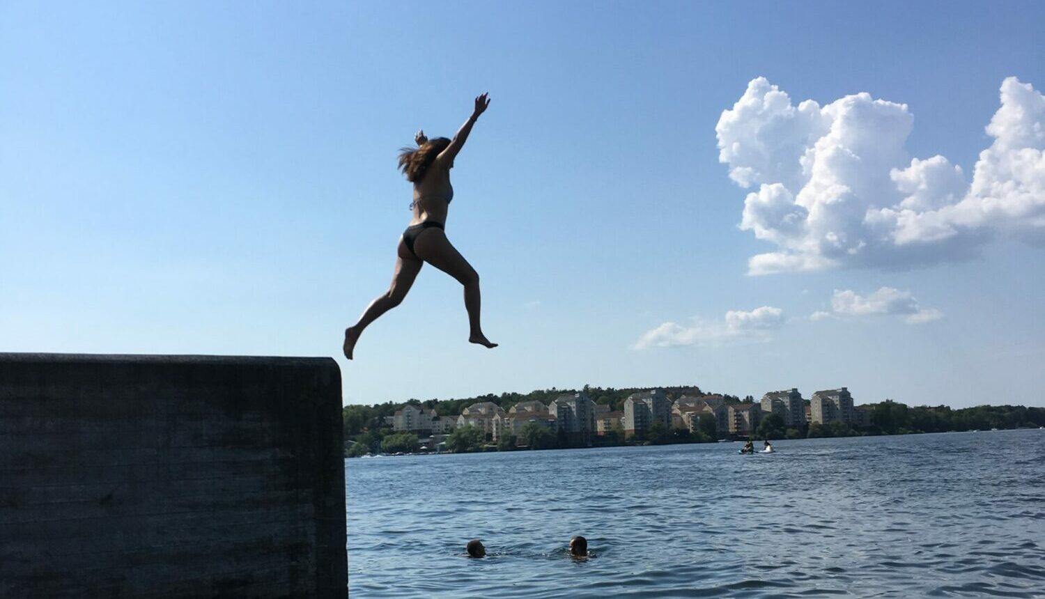 Tjej som hoppar i sjön från en hög pir