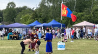 två män brottas på gräsplan under mongolisk flagga och åskådande nationaldagsfirare