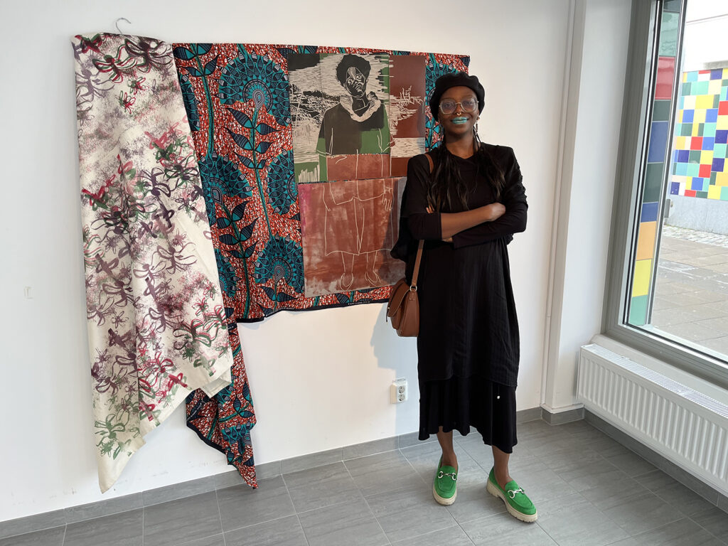 kvinna står framför sitt konstverk gjort av textilstycken och tryck