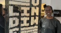 kvinna står till höger om ett konstverk med en slags väv av pärlor och namnet "U-Lindiwe"