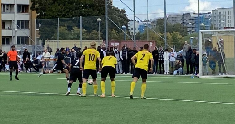 Några män spelar fotboll på en plan utomhus, en spelare slår en straff