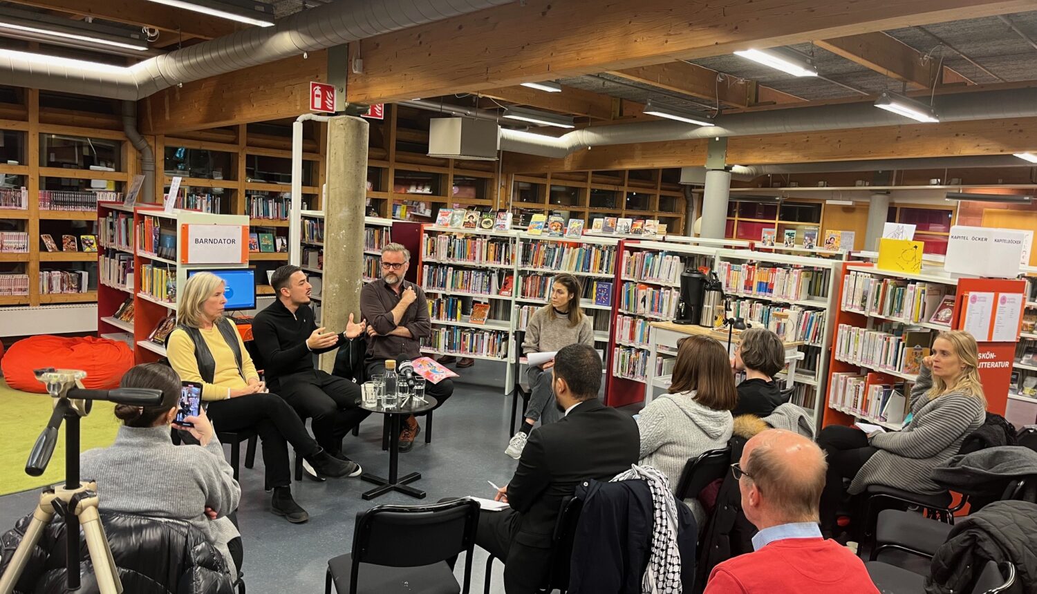 Fyrapersoner i en panel, framför en publik inne på ett bibliotek.