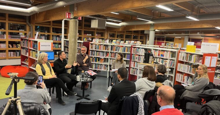 Fyrapersoner i en panel, framför en publik inne på ett bibliotek.