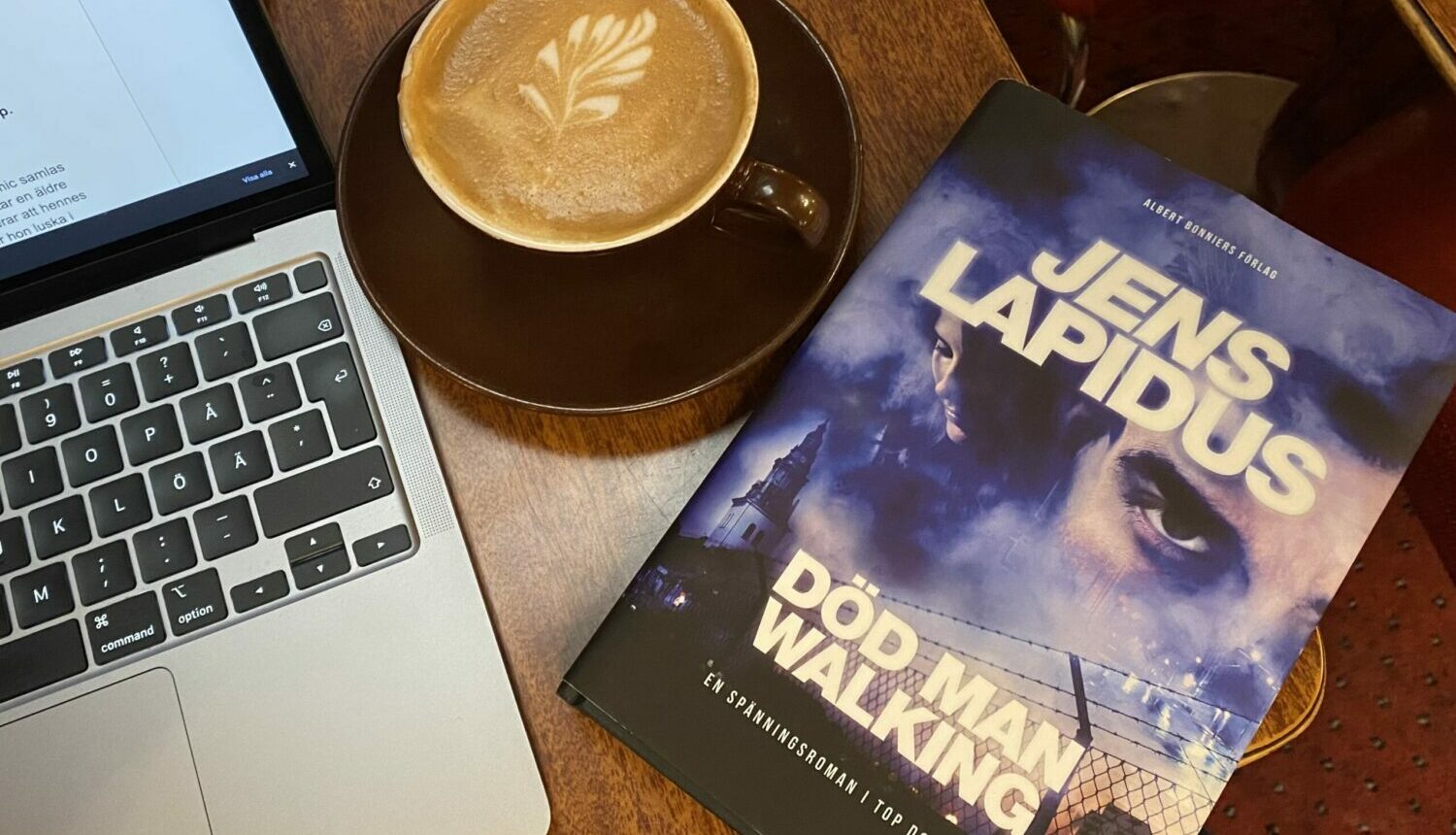 En laptop, en bok och en kopp kaffe på ett cafébord