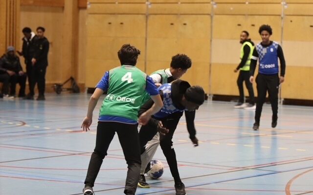 Några spelare kämpar om bollen i en fotbollsmatch i en idrottshall.