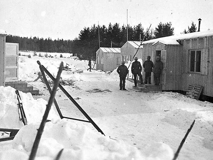 Svartvit bild från kriget, när Sverige hade interneringsläger i Storsien. Några män utanför en barack i.