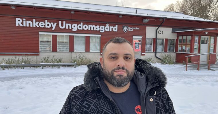 man står i svart vinterjacka framför en röd byggnad