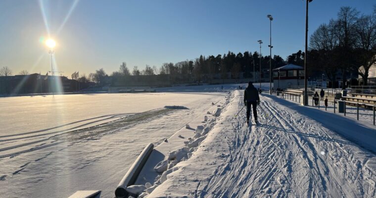 Strålande sol en vinterdag, massor med snö och ryggen på som åker skidor i spåret på Spånga IP.