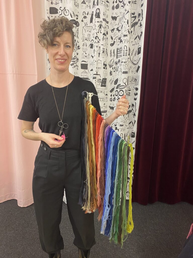Kvinna som står och håller en trådgalje med garnlängder o olika färger