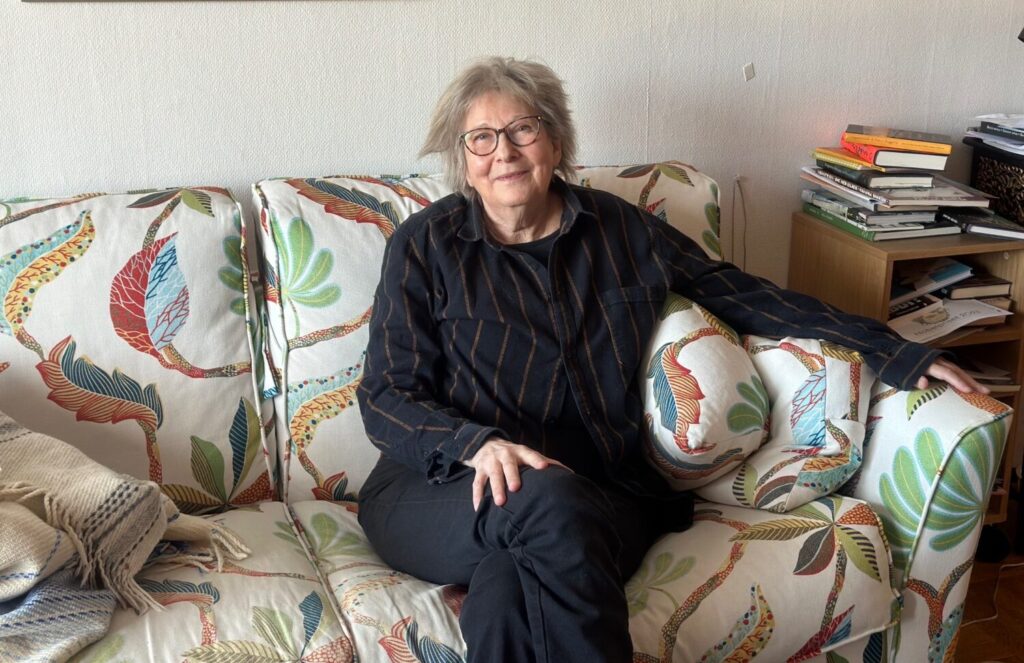 En äldre kvinna i svarat kläder sitter i en blommig soffa