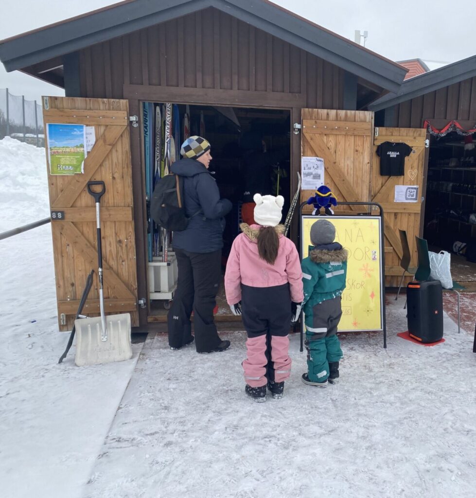 En vuxen och två barn står och tittar in i en bod full med skidor