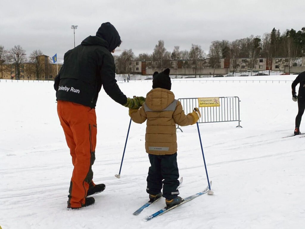ett barn på skidor får instruktioner av en ungdom i rinkeby run-jacka