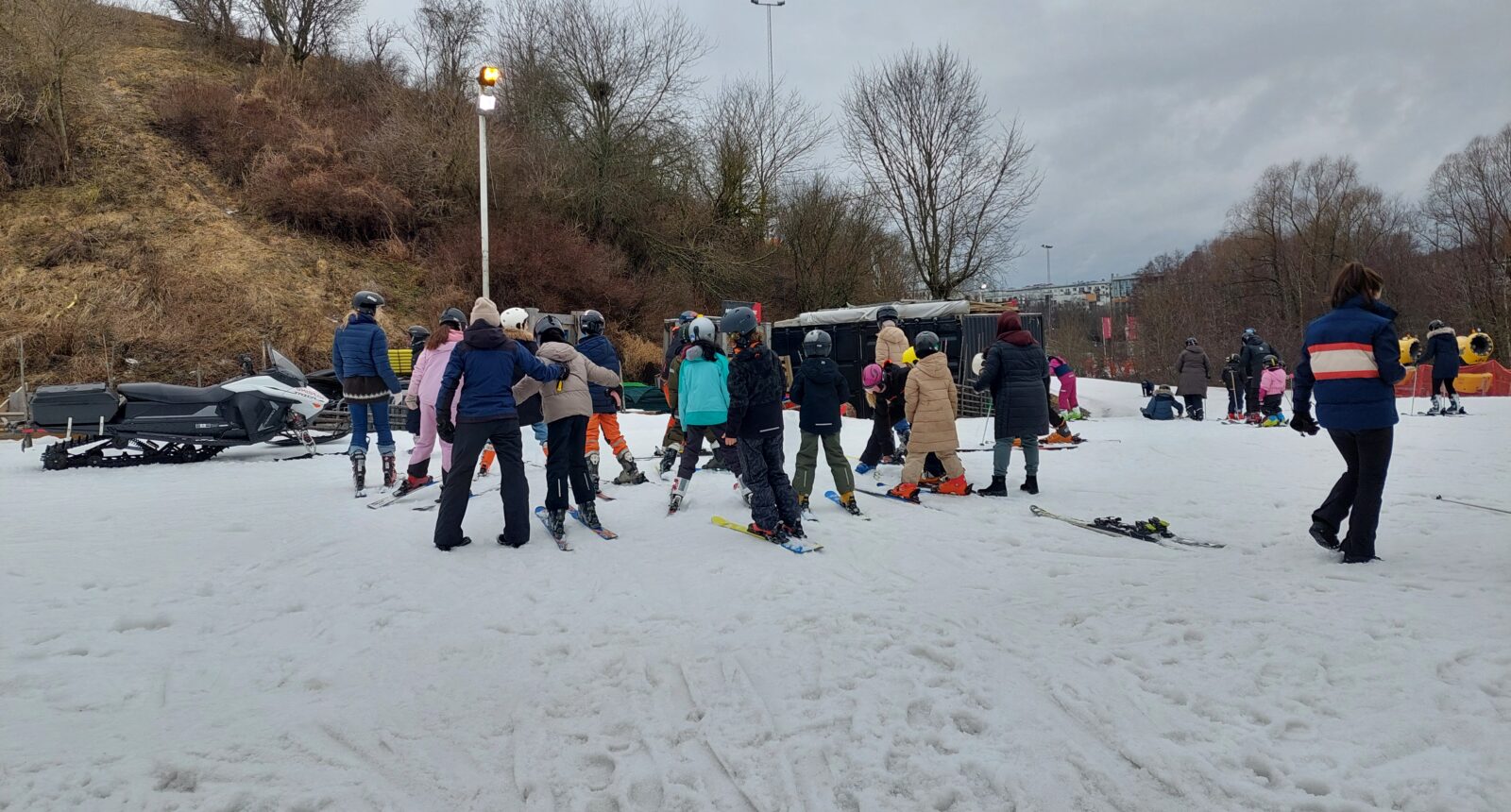 En stor grupp unga barn och står med ryf´ggen i kameran i slalombacken.