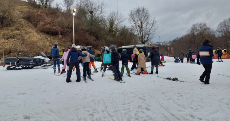En stor grupp unga barn och står med ryf´ggen i kameran i slalombacken.