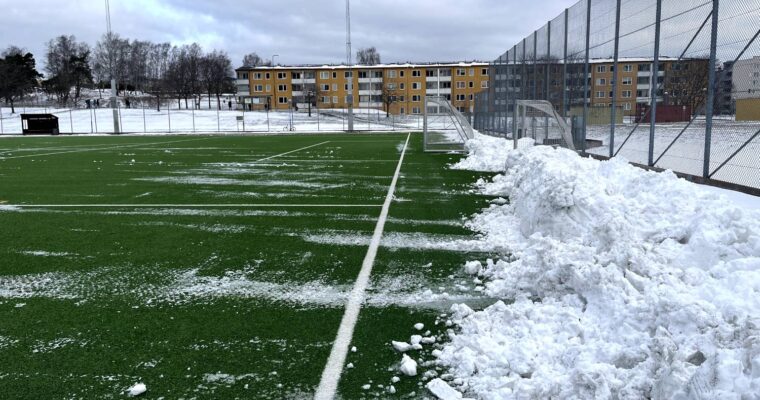 En grön plastgräsplan med snövallar längs sidorna.