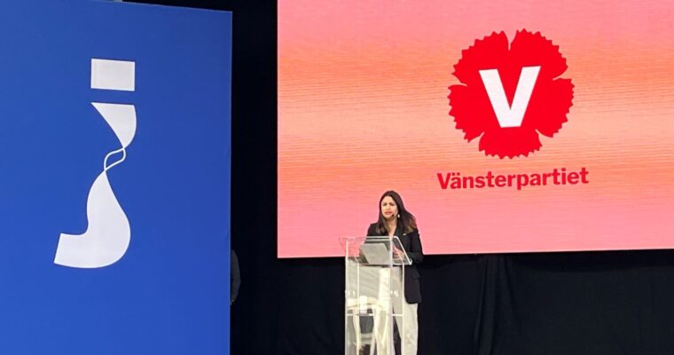 kvinna talar på stor scen framför skärmar med logotyper för Järvaveckan och Vänsterpartiet