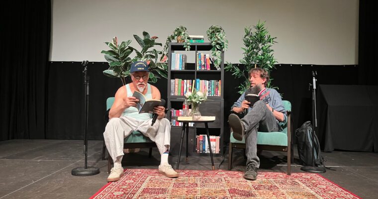 Två män på en scen, den ena läser ur en bok.