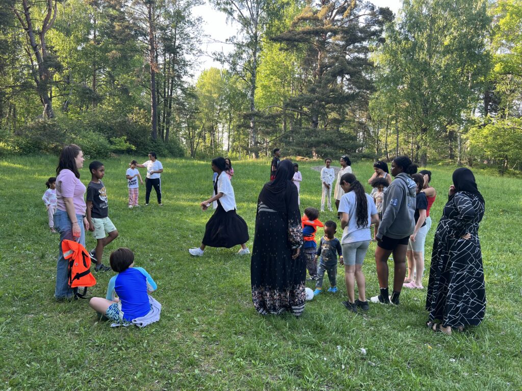 Barn och vuxna på en grön sommaräng.