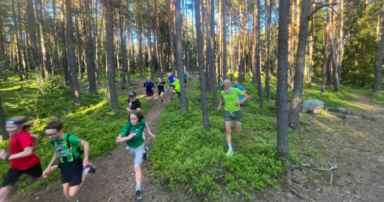 Löpare som springer emot kameran i en grön och solig skog.