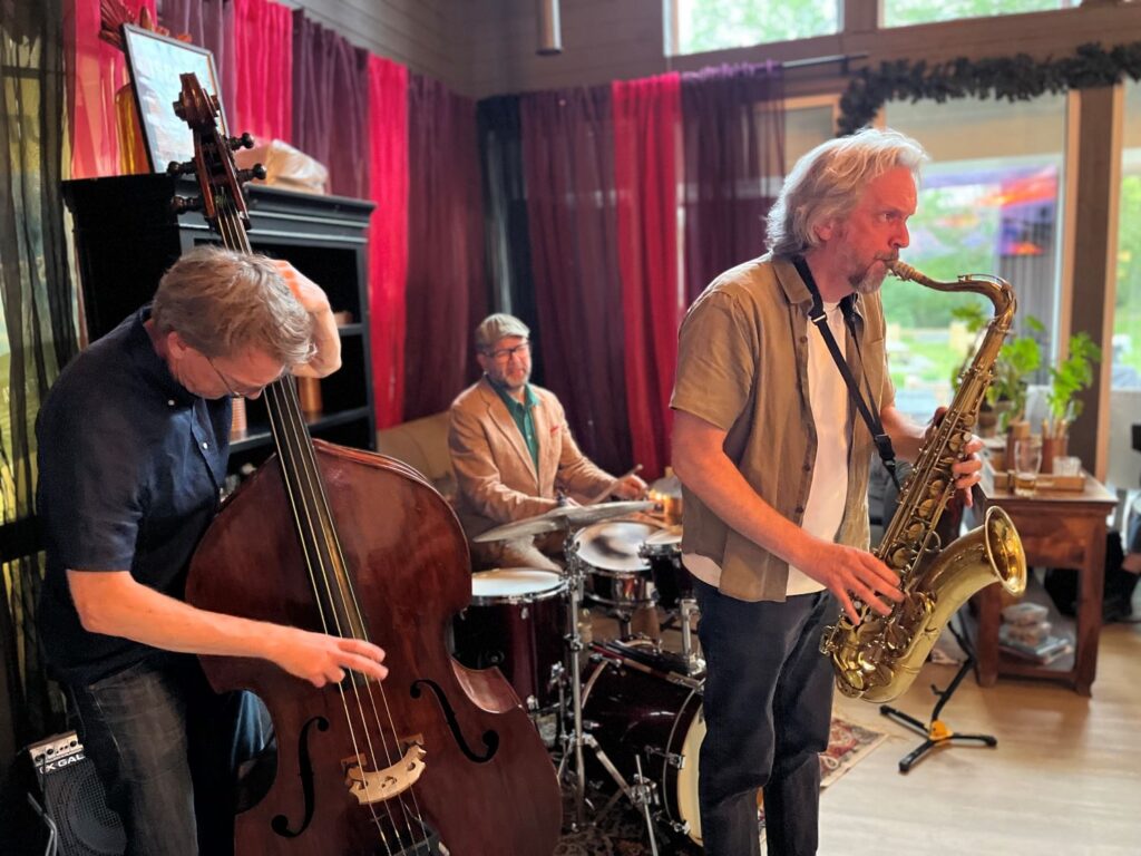 tre män, en på kontrabas, en på saxofon och en på trummot, spelar live inomhus