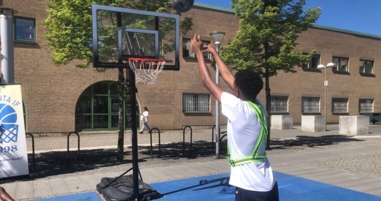 ung man kastar basketboll mot korg på torget