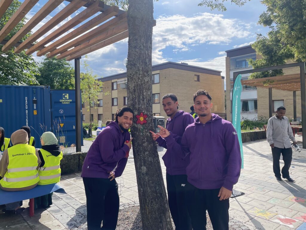 Tre unga män som spexar och pekar på en målad blomma på en trädstam-