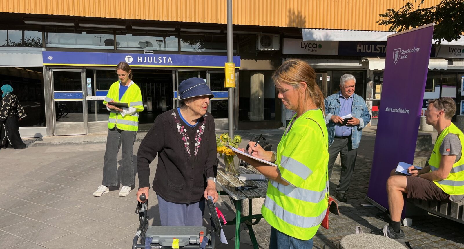 Tre personer i gula västar frågar folk på torget-